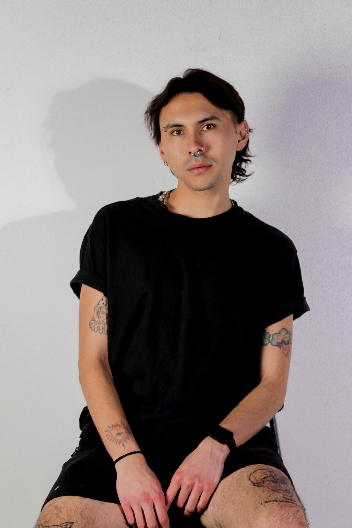 Minimal portrait in black clothing with a visible septum ring and ear piercings