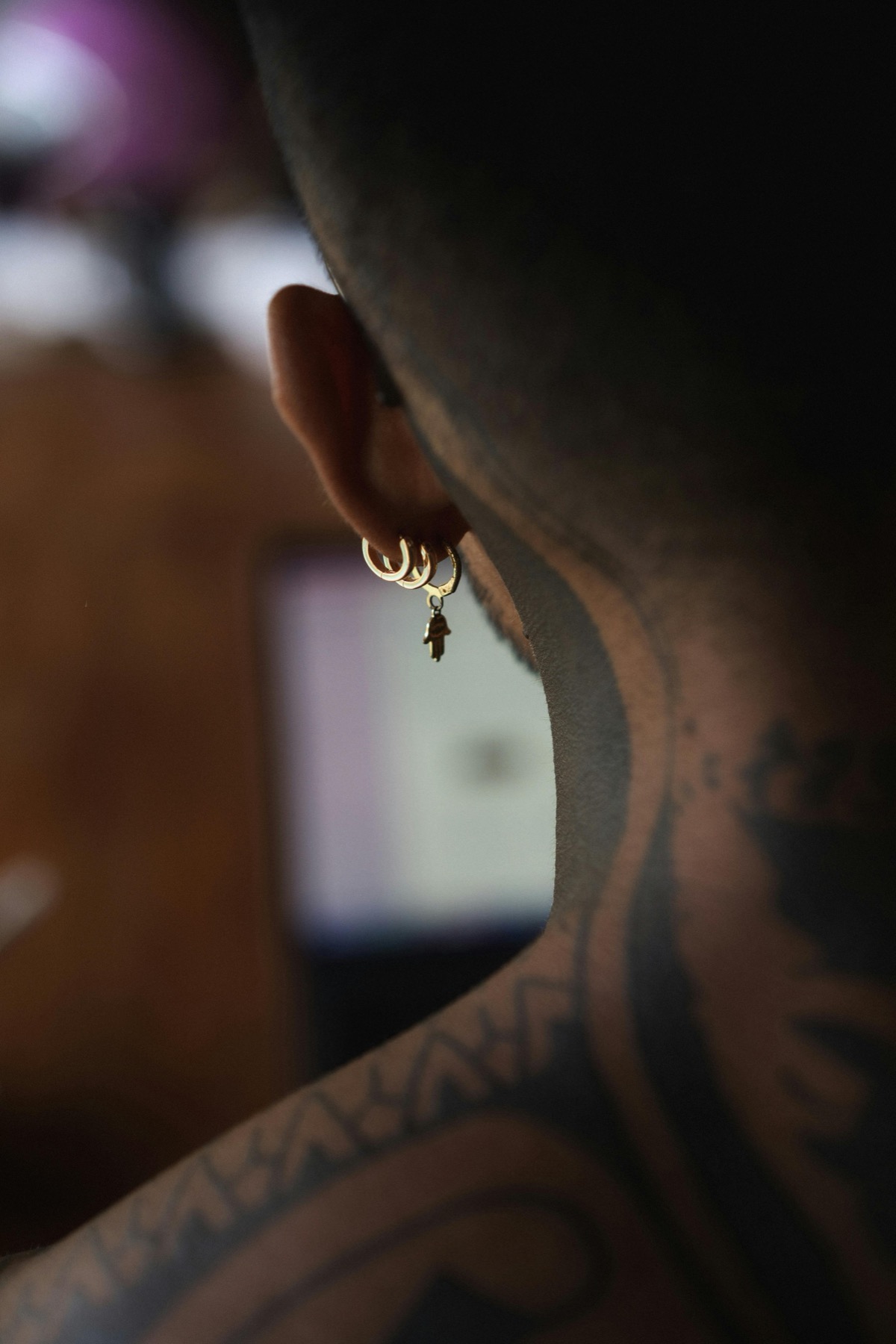 Back-of-neck portrait with multiple hoop earrings and a tattooed neck
